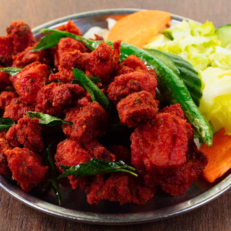 Crispy deep-fried South Indian Chicken 65 appetizer garnished with curry leaves and onions at Karaikudi Chettinad Restaurant