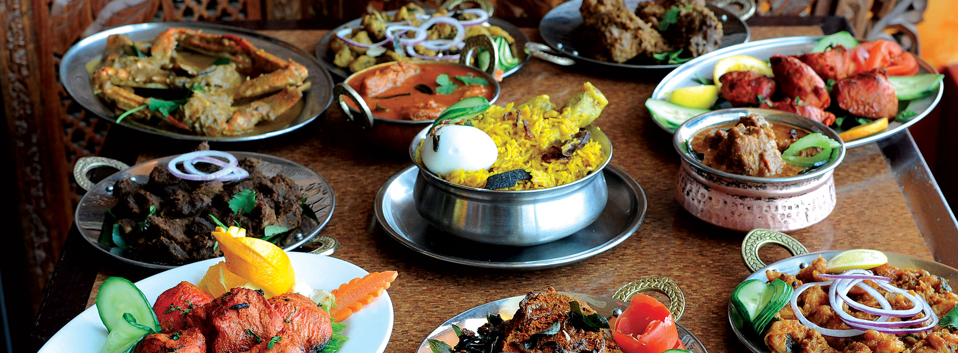 A diverse family dinner spread of South Indian dosas, North Indian tandoori, and traditional meat curries at Karaikudi Restaurant in Toronto